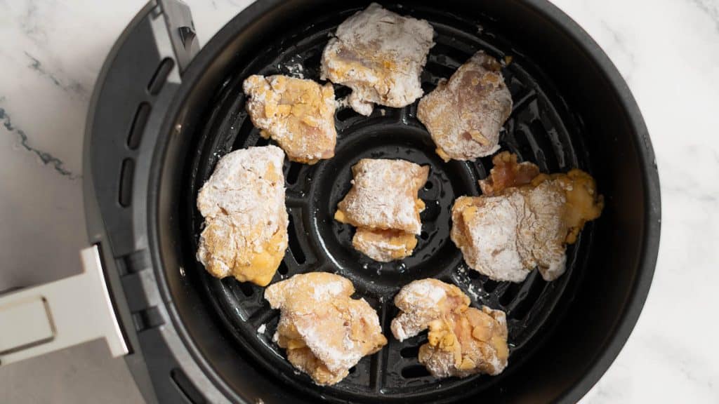 Pieces of chicken thigh coated in potato starch in an air fryer basket