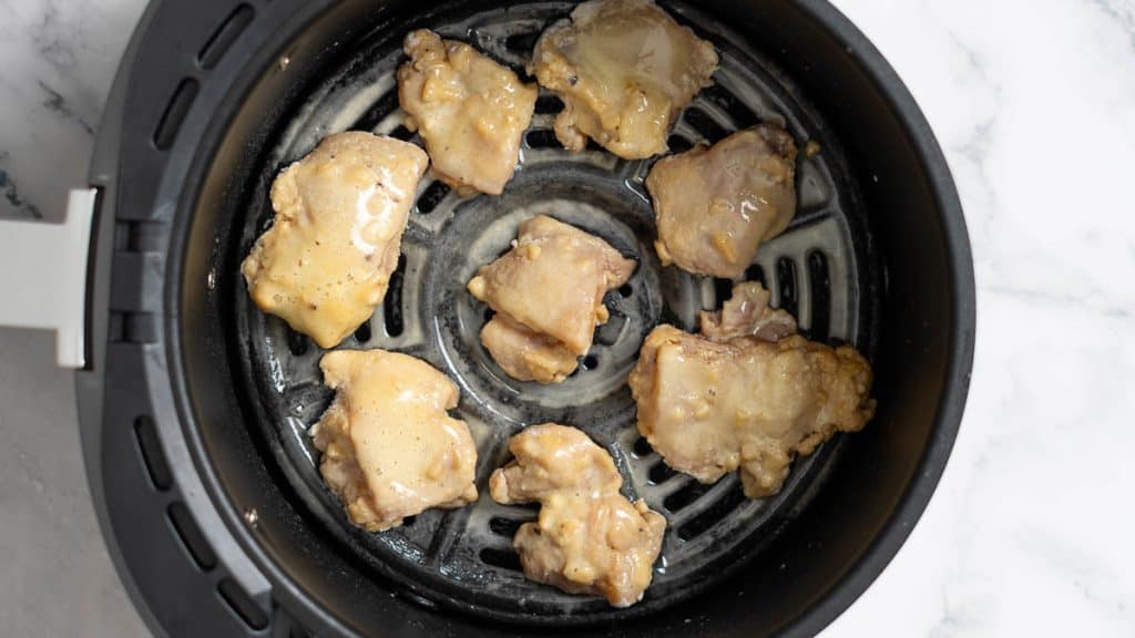 Partially cooked chicken thigh in an air fryer basket