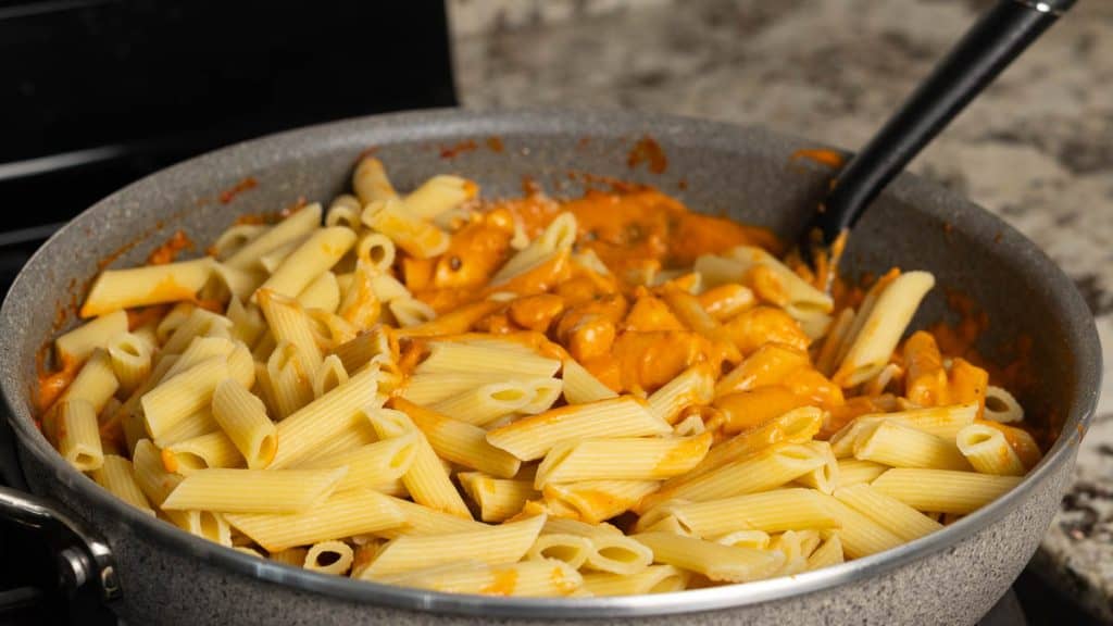 Mixing creamy pasta sauce with penne pasta