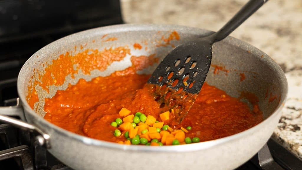 Stirring in frozen peas and carrots into tomato sauce