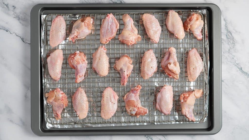 Seasoned raw chicken wings on a baking rack on a baking sheet