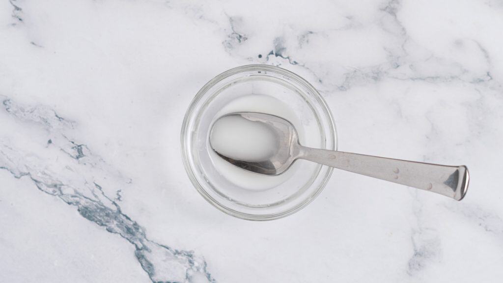 Cornstarch slurry in a glass bowl with a stainless steel spoon