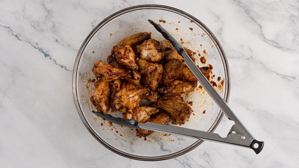 Baked chicken wings coated in soy garlic sauce in a bowl with tongs
