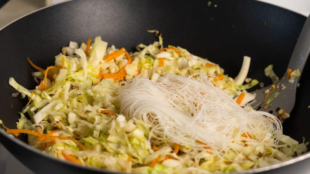 Rice vermicelli on top of sliced cabbage and carrots in a pan