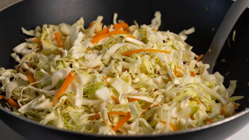 Sliced raw cabbage with julienned carrots and minced shiitake mushrooms in a pan