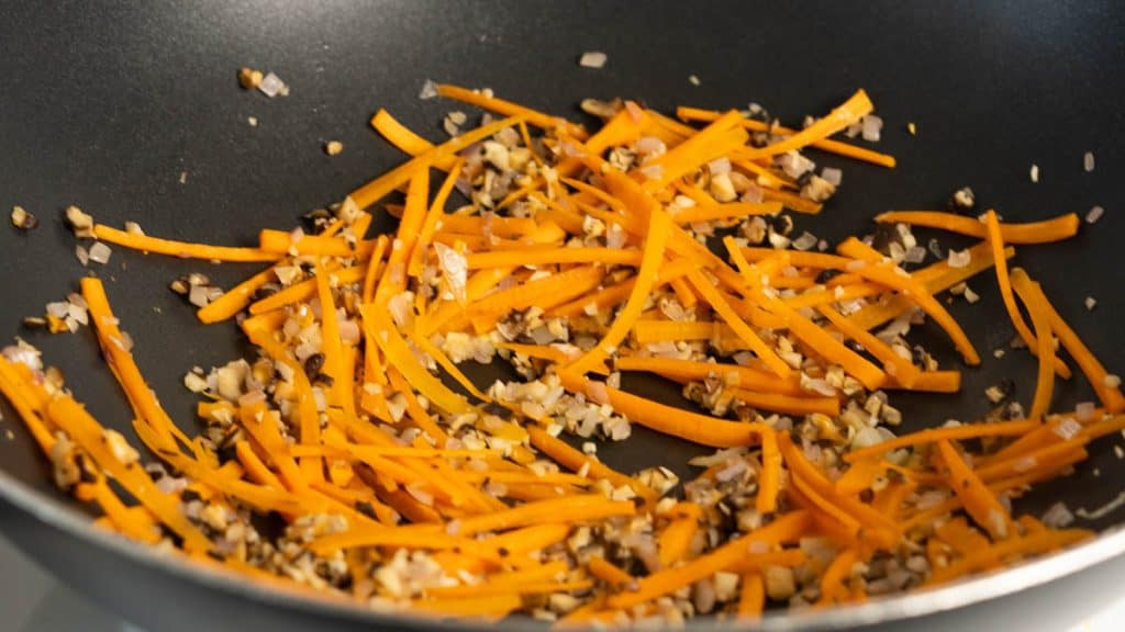 Stir-fried julienned carrots and minced mushrooms in a pan