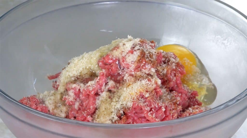 Ground beef in a glass bowl with ingredients for Japanese Hamburg steak