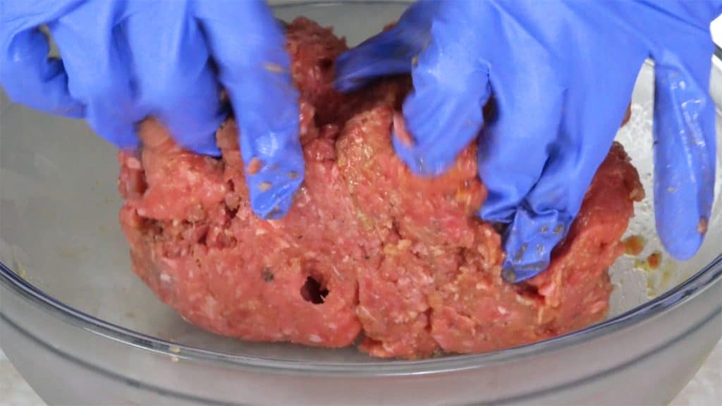 Mixing ground beef with gloved hands in a glass bowl