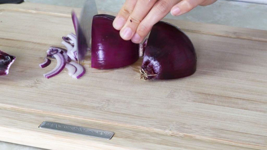 Slicing red onion on a wooden cutting board with a knife