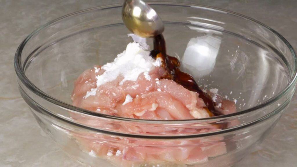 Sliced raw chicken breast in a glass bowl topped with cornstarch, salt, and soy sauce