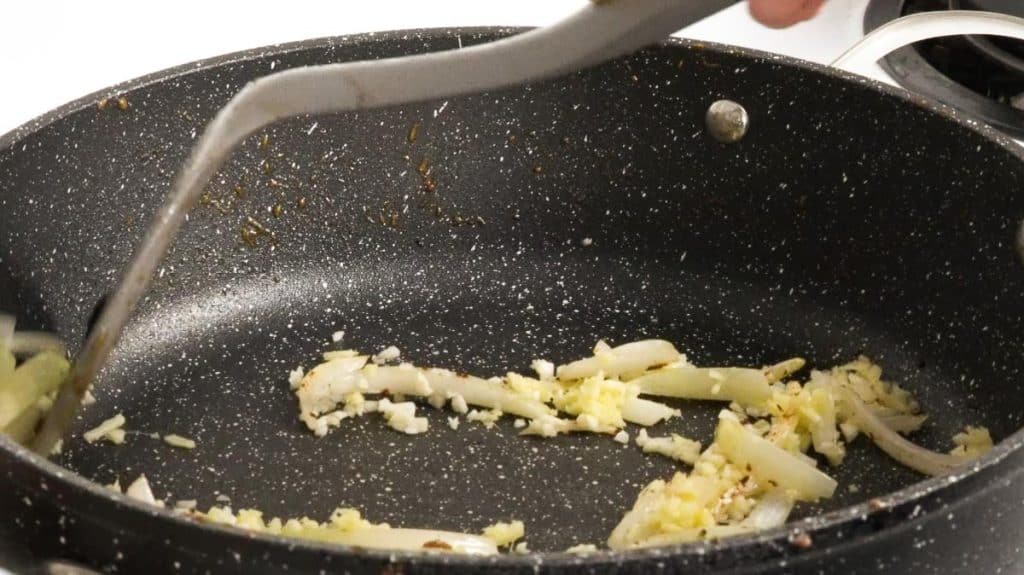 Stir frying minced onions, garlic and ginger on a black non-stick pan with a spatula