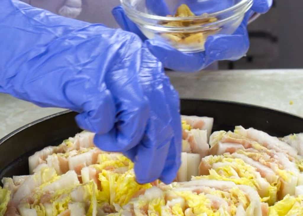 Putting slices of ginger and garlic in between layers of napa cabbage and pork belly in a Dutch oven