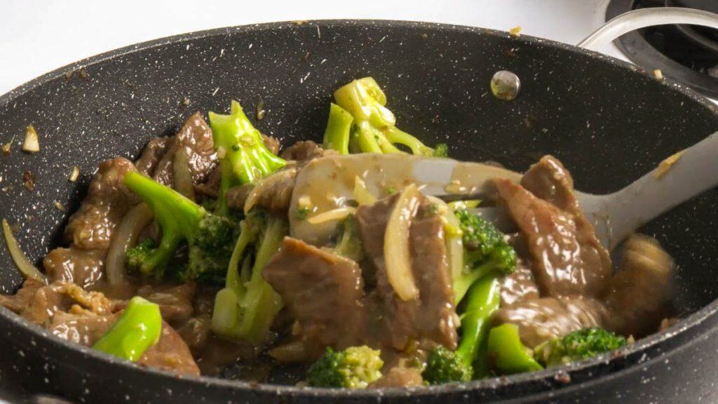 Stir frying beef and broccoli in a black non-stick pan with a silicone spatula