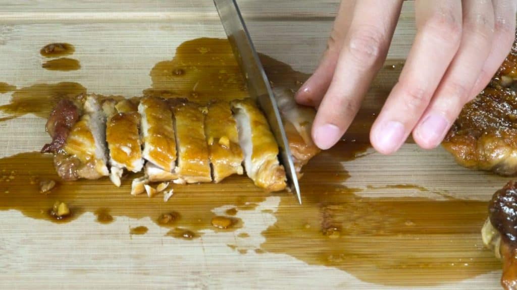 Slicing teriyaki chicken with a knife on a wooden cutting board