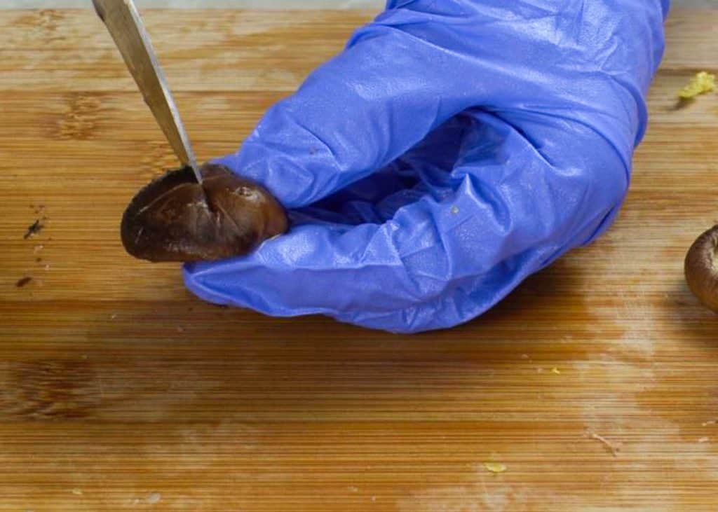 Scoring a shiitake mushroom with a knife on a wooden cutting board