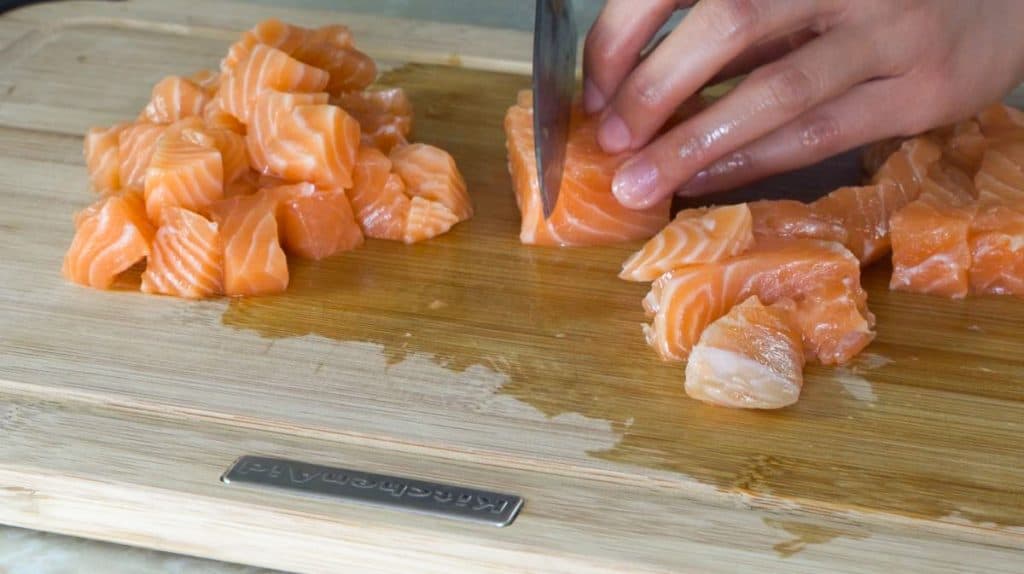 Dicing raw salmon with a knife on a wooden cutting board