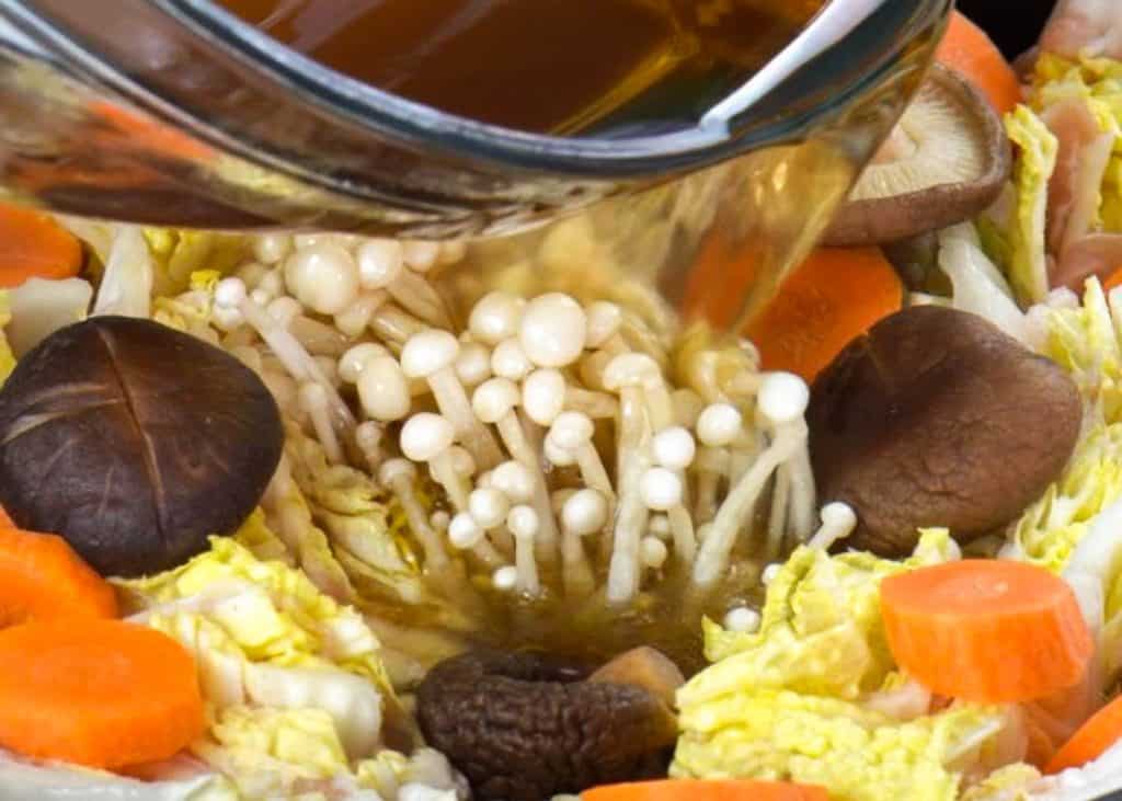 Pouring brown soup from a glass bowl into the mille feuille nabe