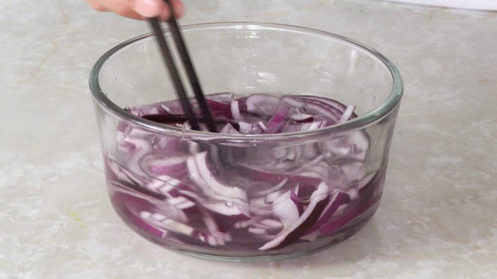 Mixing red onion slices in pickling solution in a glass bowl with chopsticks