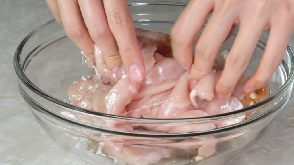 Mixing sliced raw chicken breast with cornstarch, soy sauce and salt