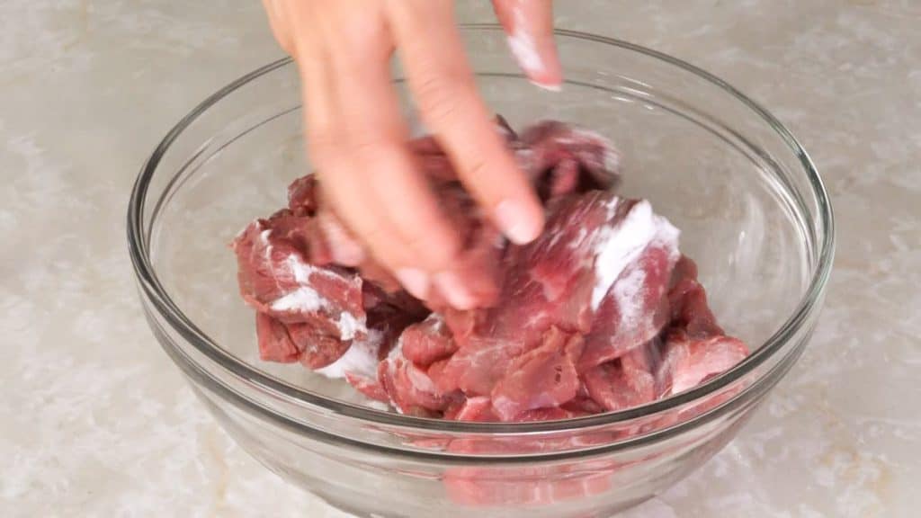 Mixing sliced beef sirloin with baking soda in a glass bowl