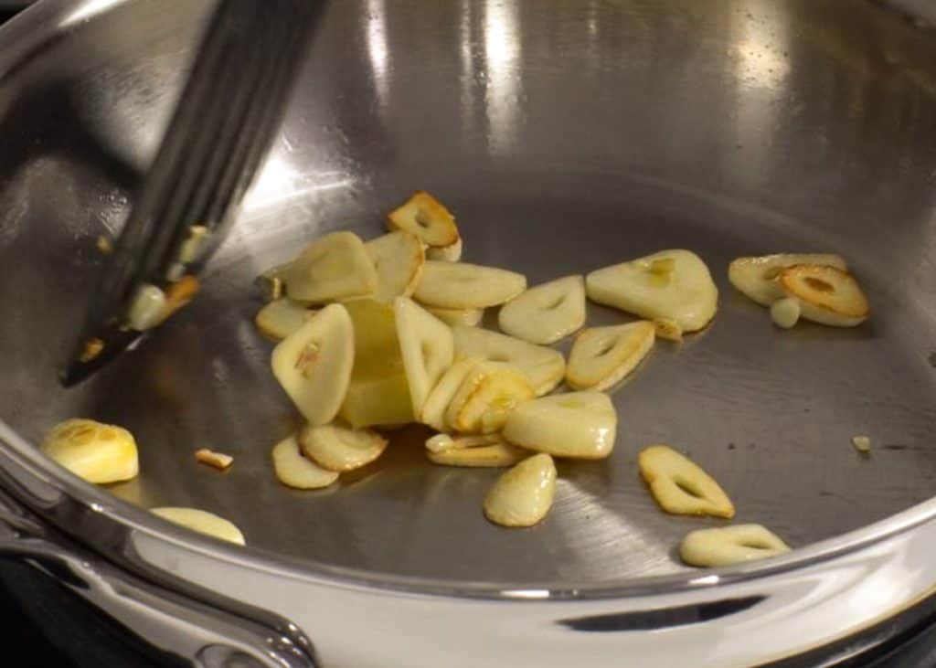 Frying sliced ginger and garlic on a stainless steel skillet