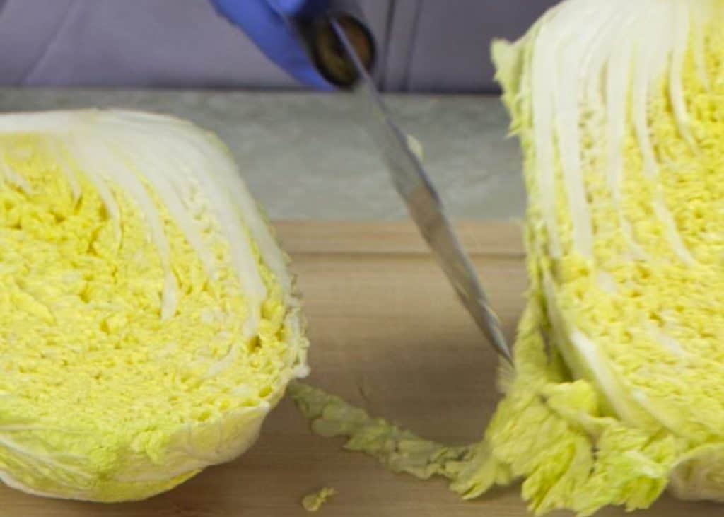 Slicing napa cabbage in half on a wooden cutting board