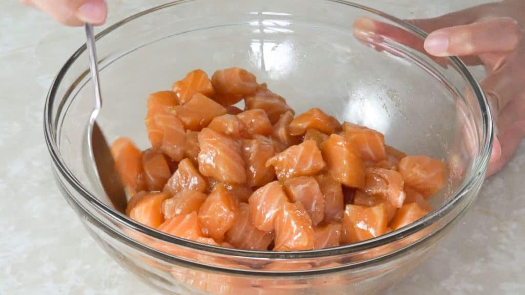 Mixing diced raw salmon with marinade ingredients in a glass bowl