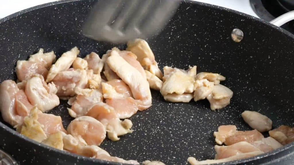 Cooking sliced raw chicken breast on a non-stick pan with a spatula