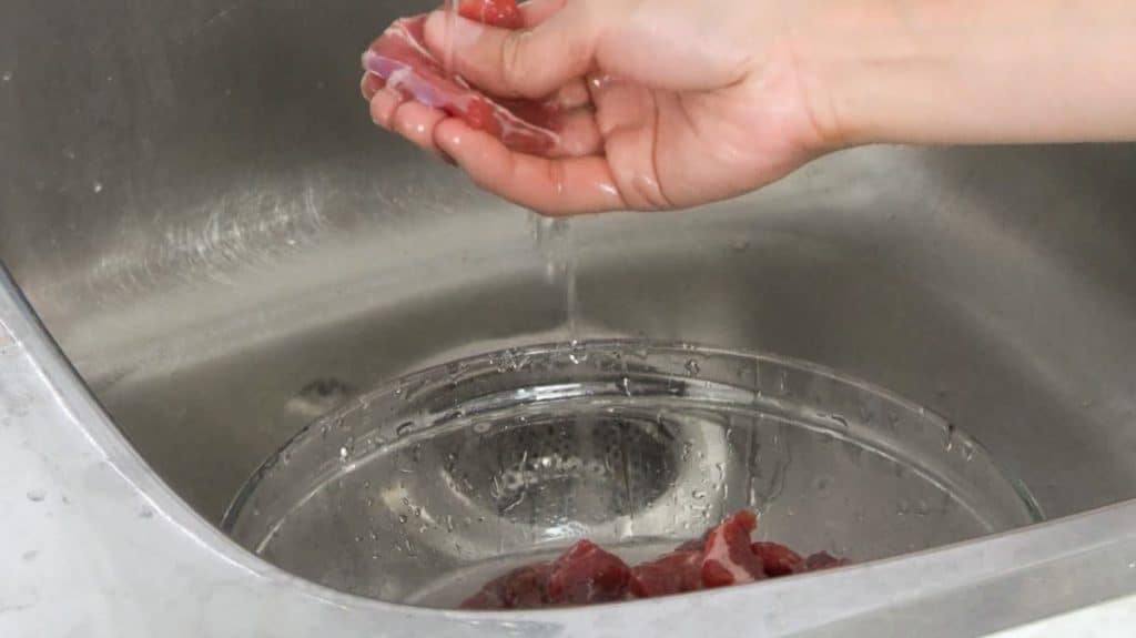 Rinsing a slice of beef sirloin under running cold water in a sink
