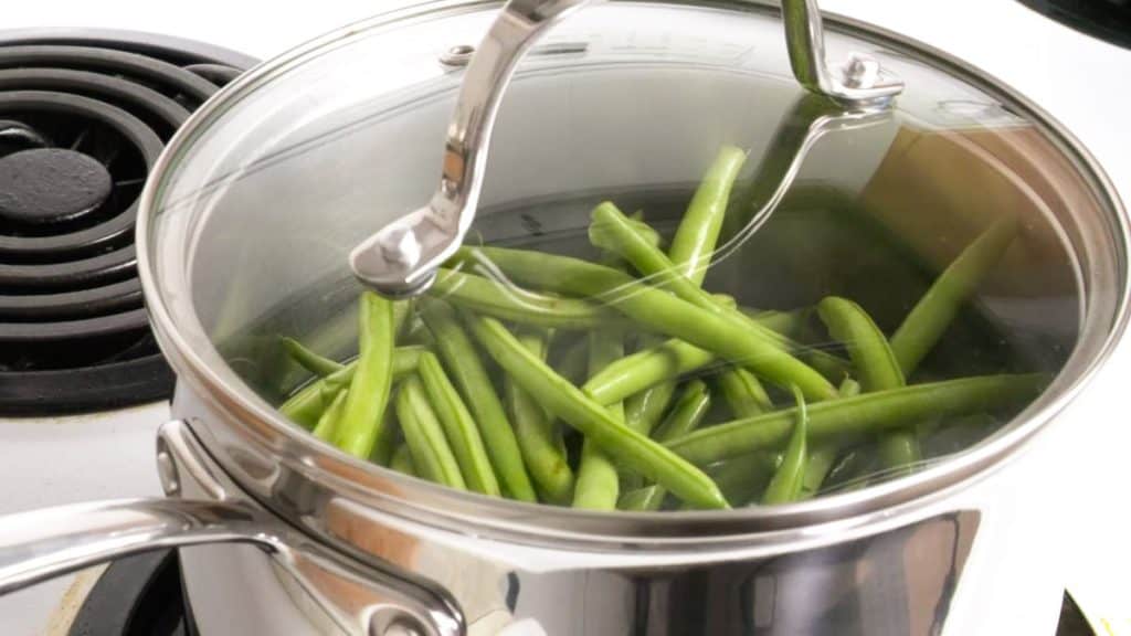 Partially blanching and steaming green beans in a stainless steel sauce pan on an electric stove