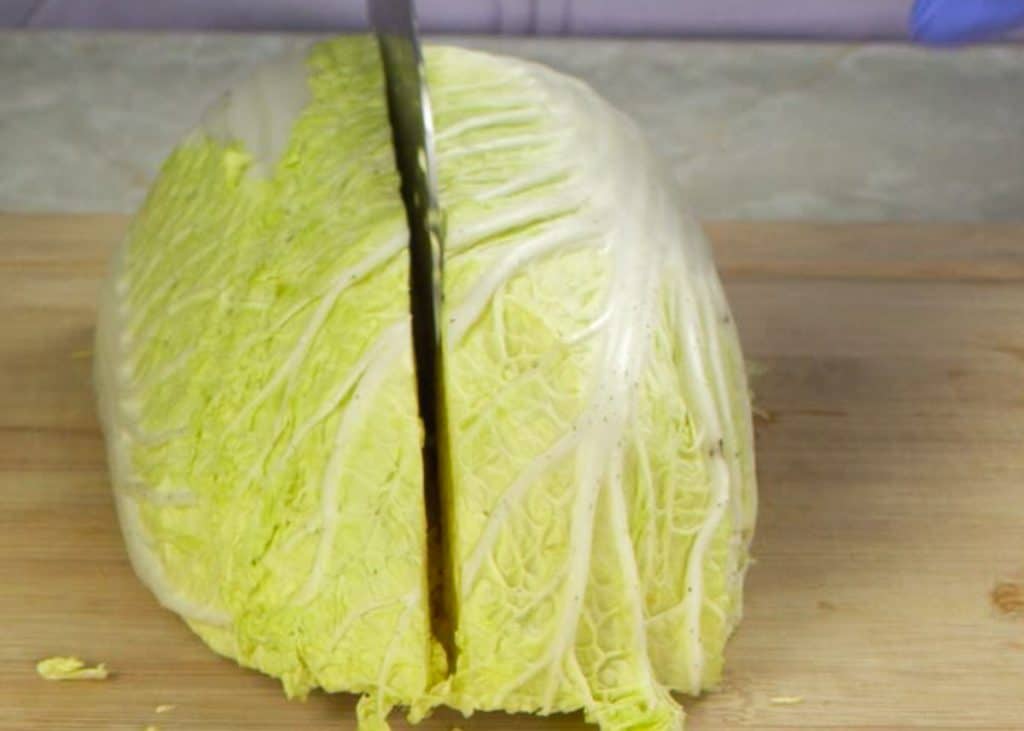 Slicing napa cabbage into quarters on a wooden cutting board