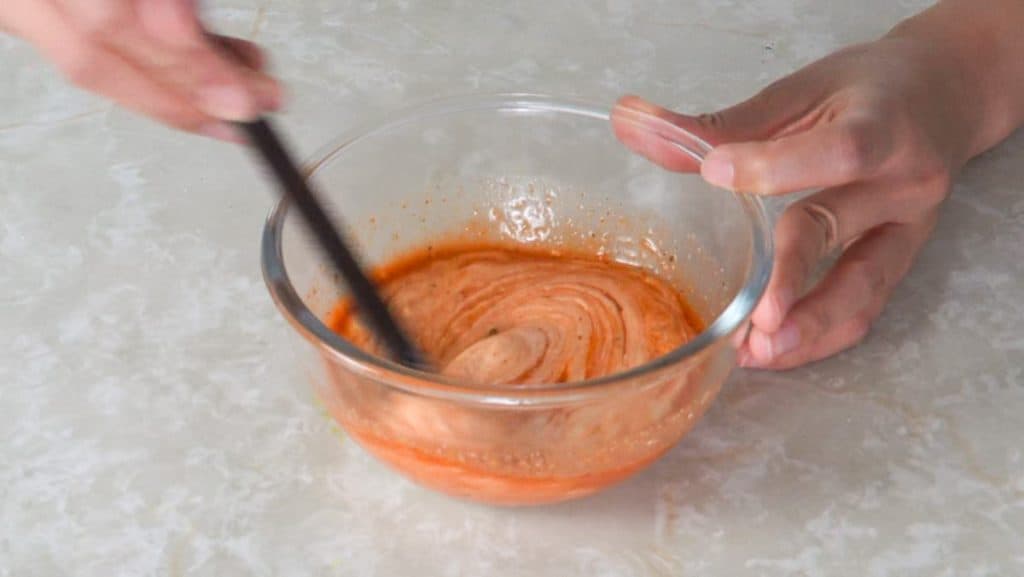 Mixing spicy mayo ingredients with chopsticks in a small glass bowl
