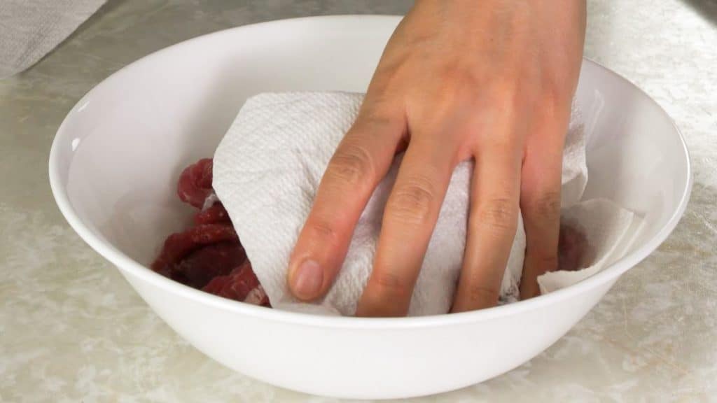 Patting dry beef slices in a white bowl with a paper towel