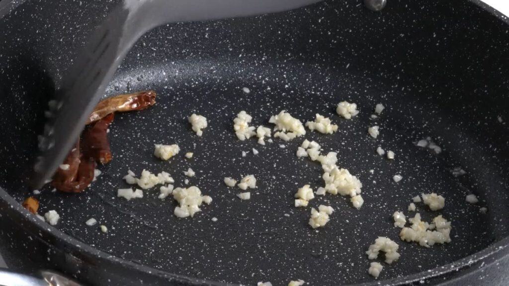 Frying minced garlic and whole dried chili peppers on a non-stick pan using a spatula