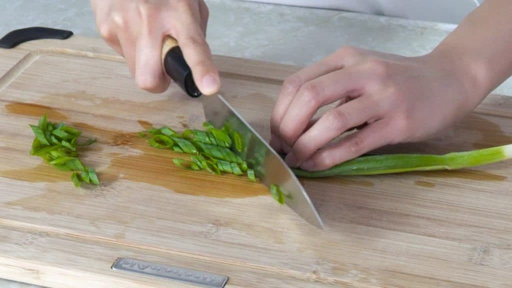 Slicing a green onion at an angle with a knife on a wooden cutting board