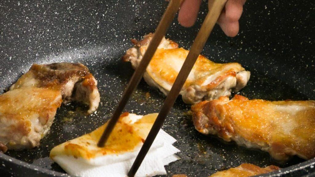 Wiping grease from chicken thighs off a non-stick pan using chopsticks and paper towel