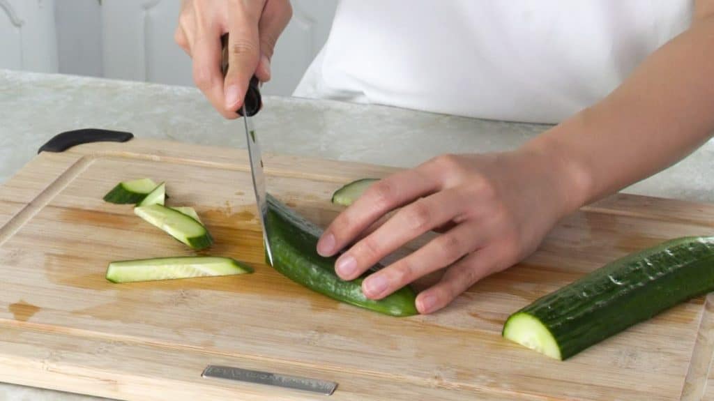Slicing cucumber with a knife on a wooden cutting board