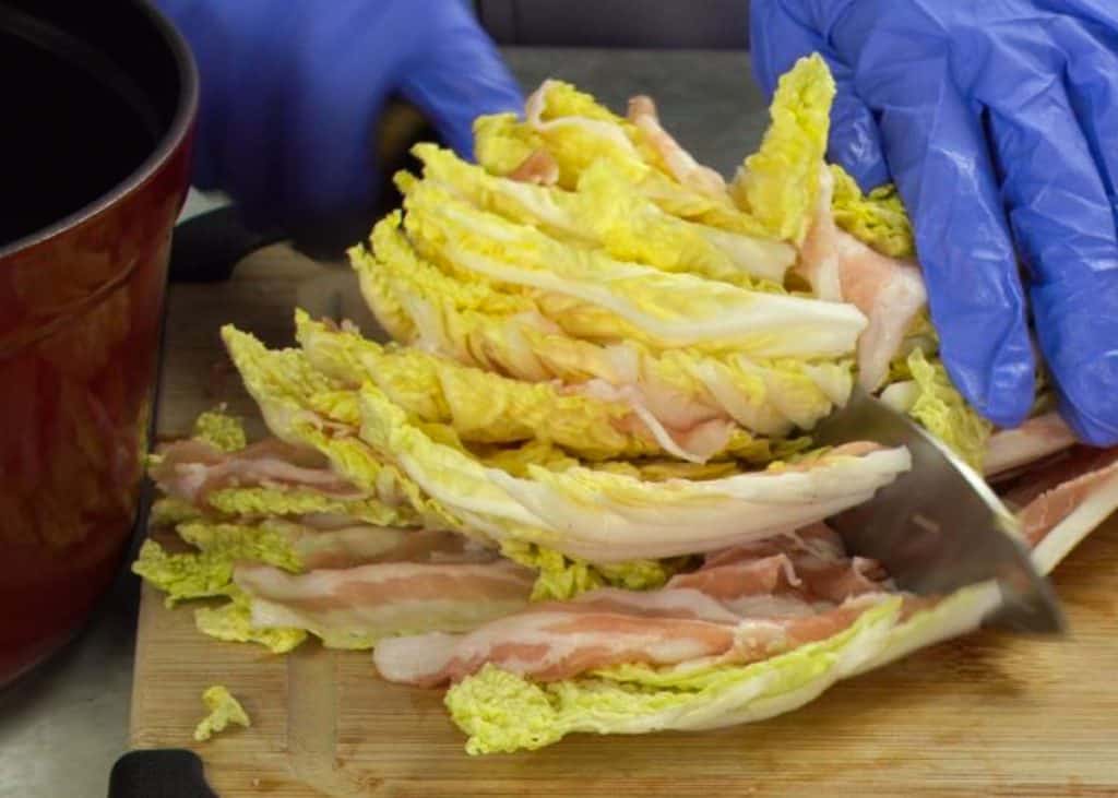 Slicing napa cabbage layered with pork belly in half with a knife on a wooden cutting board