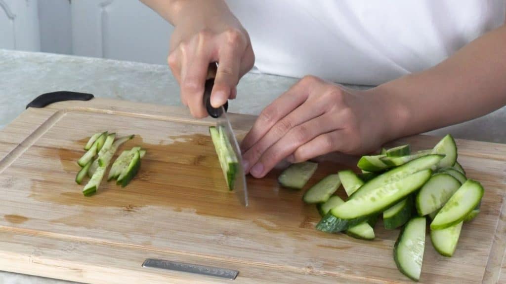 Slicing cucumber into matchsticks with a knife on a wooden cutting board