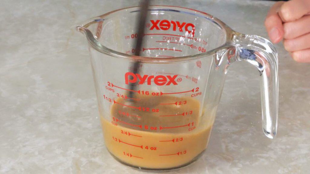 Mixing beef and broccoli marinade ingredients in a glass measuring cup with chopsticks