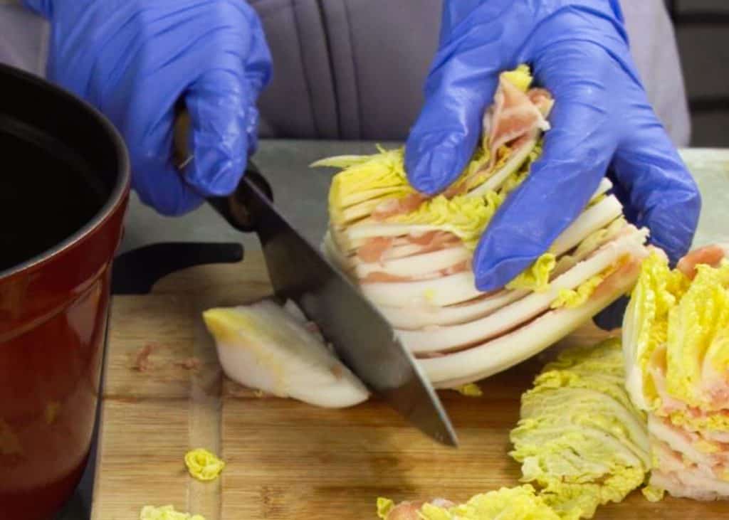 Slicing off the core of a napa cabbage layered with pork belly with a knife on a wooden cutting board