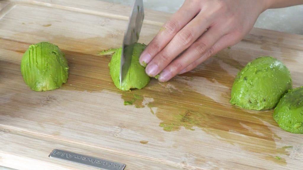 Slicing avocado halves with a knife on a wooden cutting board