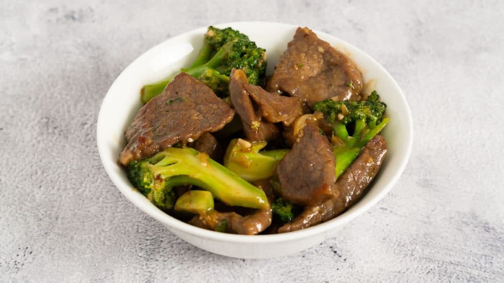 Beef and broccoli stir fry in a white bowl on a rustic surface