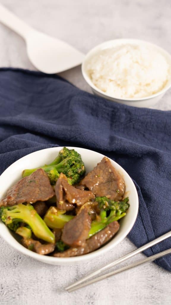 Beef and Broccoli Stir-Fry in a white bowl with a bowl of steamed white rice