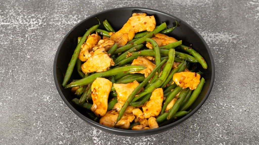 Stir-fried spicy chicken and green beans in a black bowl on a rustic surface