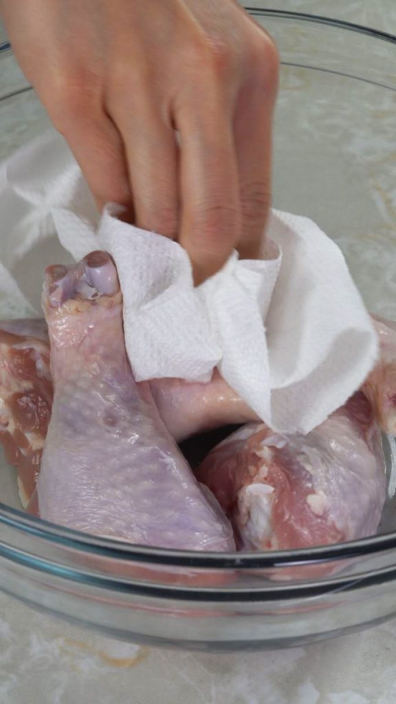 Patting chicken thighs dry with a paper towel in a glass bowl 
