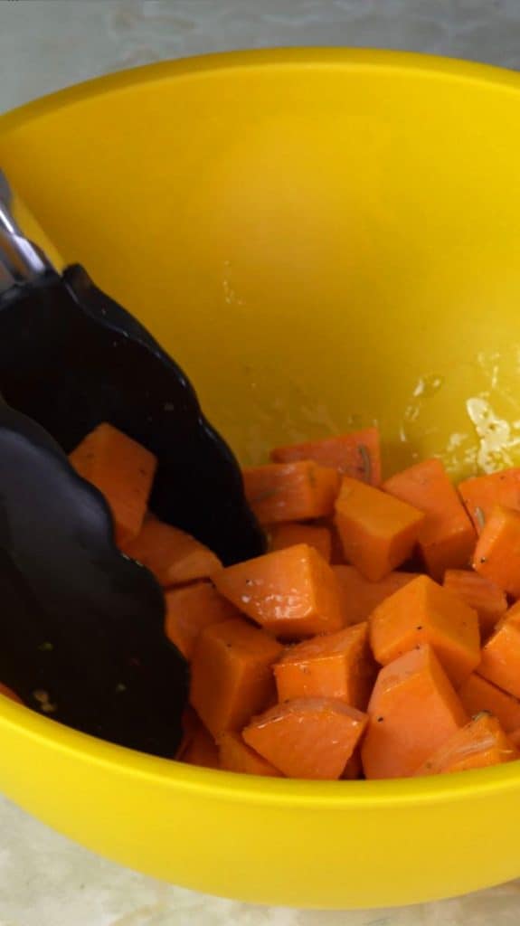 Diced sweet potato coated in oil and seasoning in a plastic yellow mixing bowl