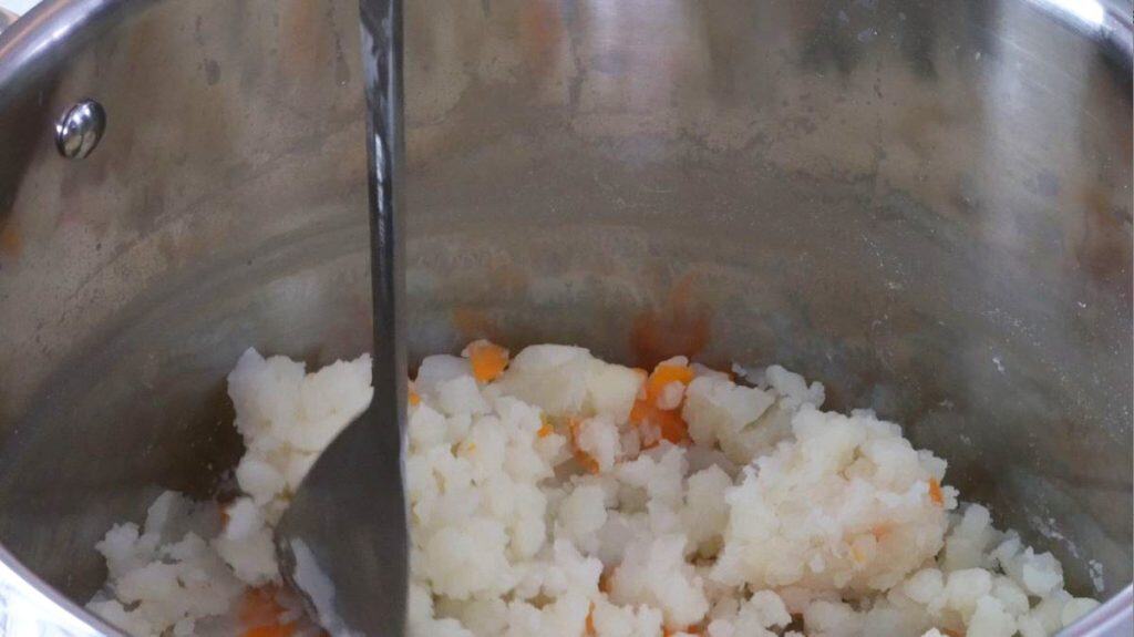 Mashing potatoes with a potato masher in a stainless steel saucepan
