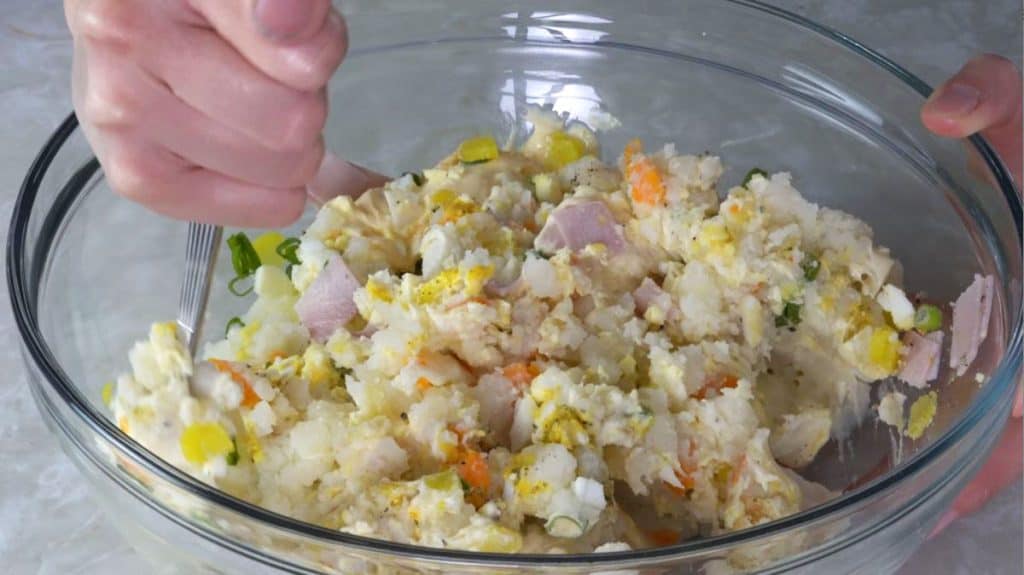 Mixing potato, ham, green onion, egg, carrot and seasonings in a glass bowl