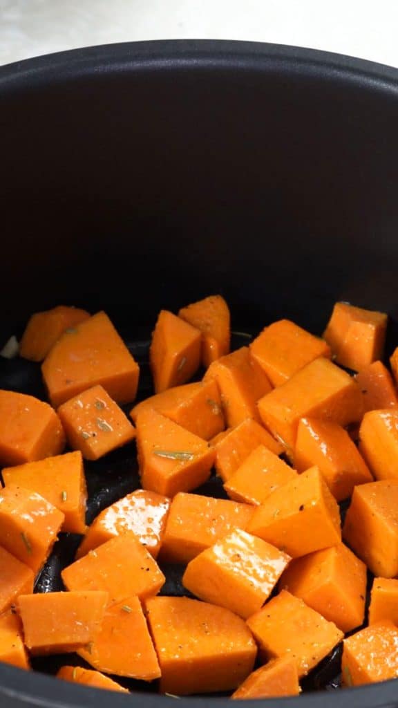 Uncooked diced sweet potato coated in oil and seasoning in an air fryer basket